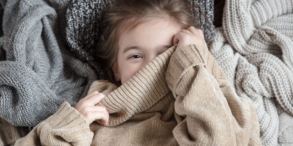 Portrait of an adorable toddler girl wearing fashion knitted clothes. Lies on backdrop of of multiple different cozy knitted sweaters. The concept of warm clothes.