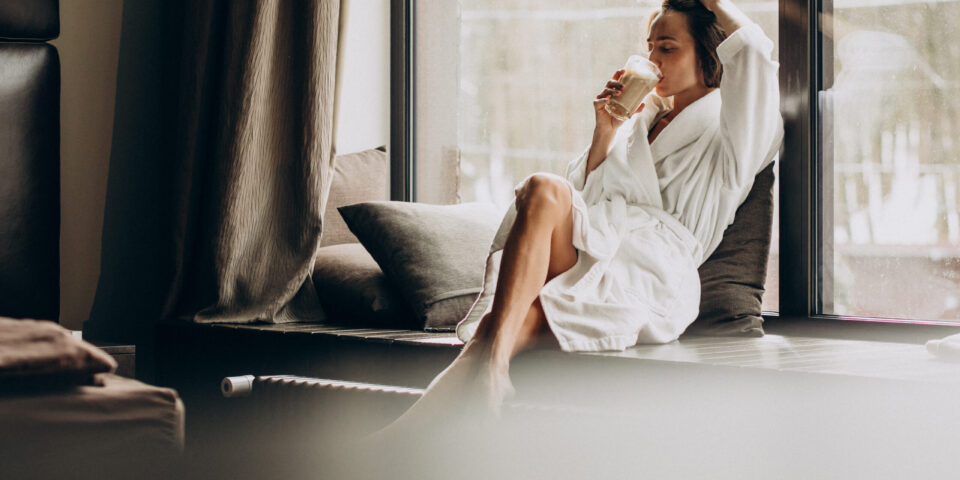 Woman drinking coffee in bathrobe by the window at home